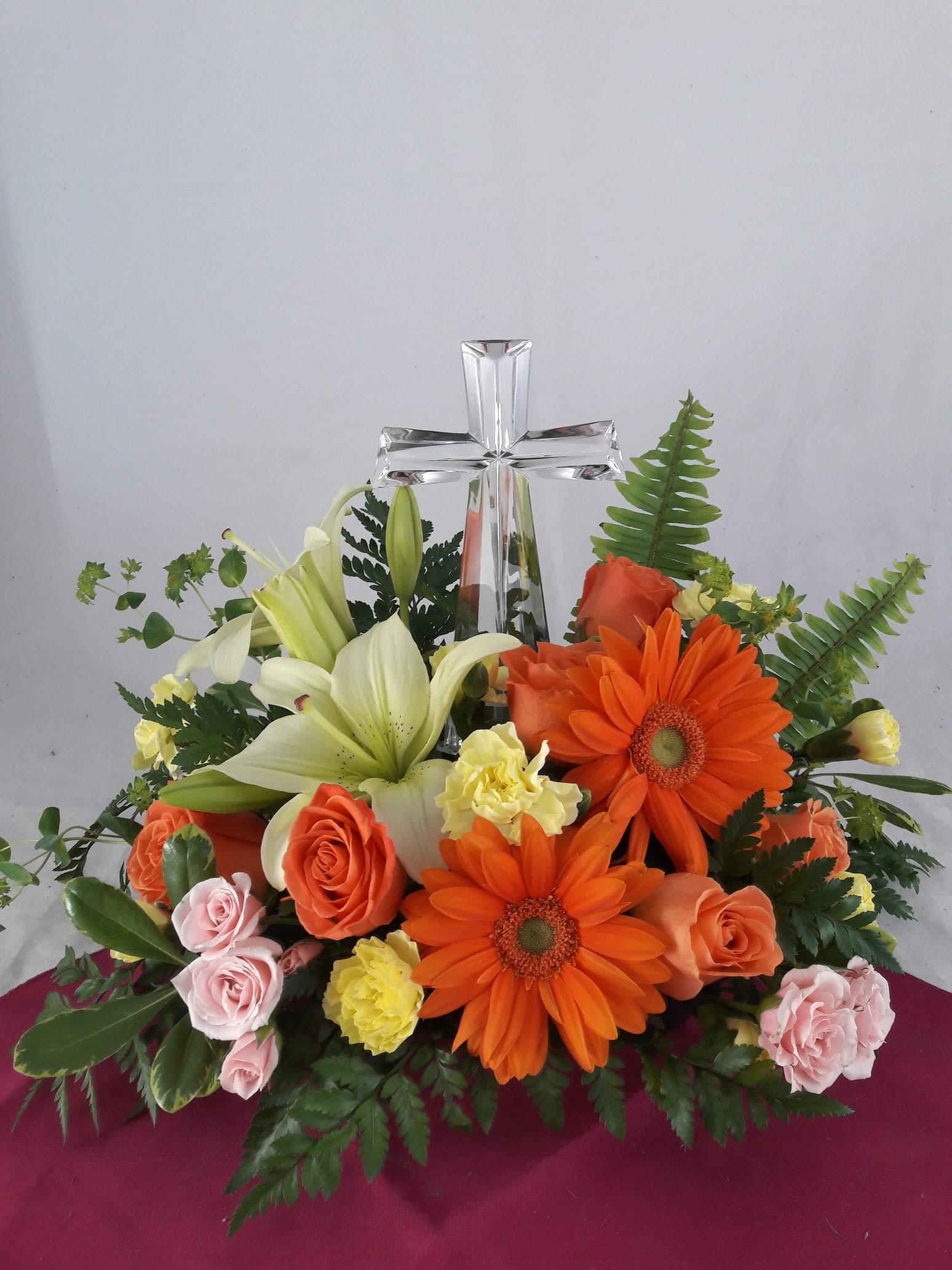 Floral arrangement with a clear glass cross and orange, white, and pink flowers