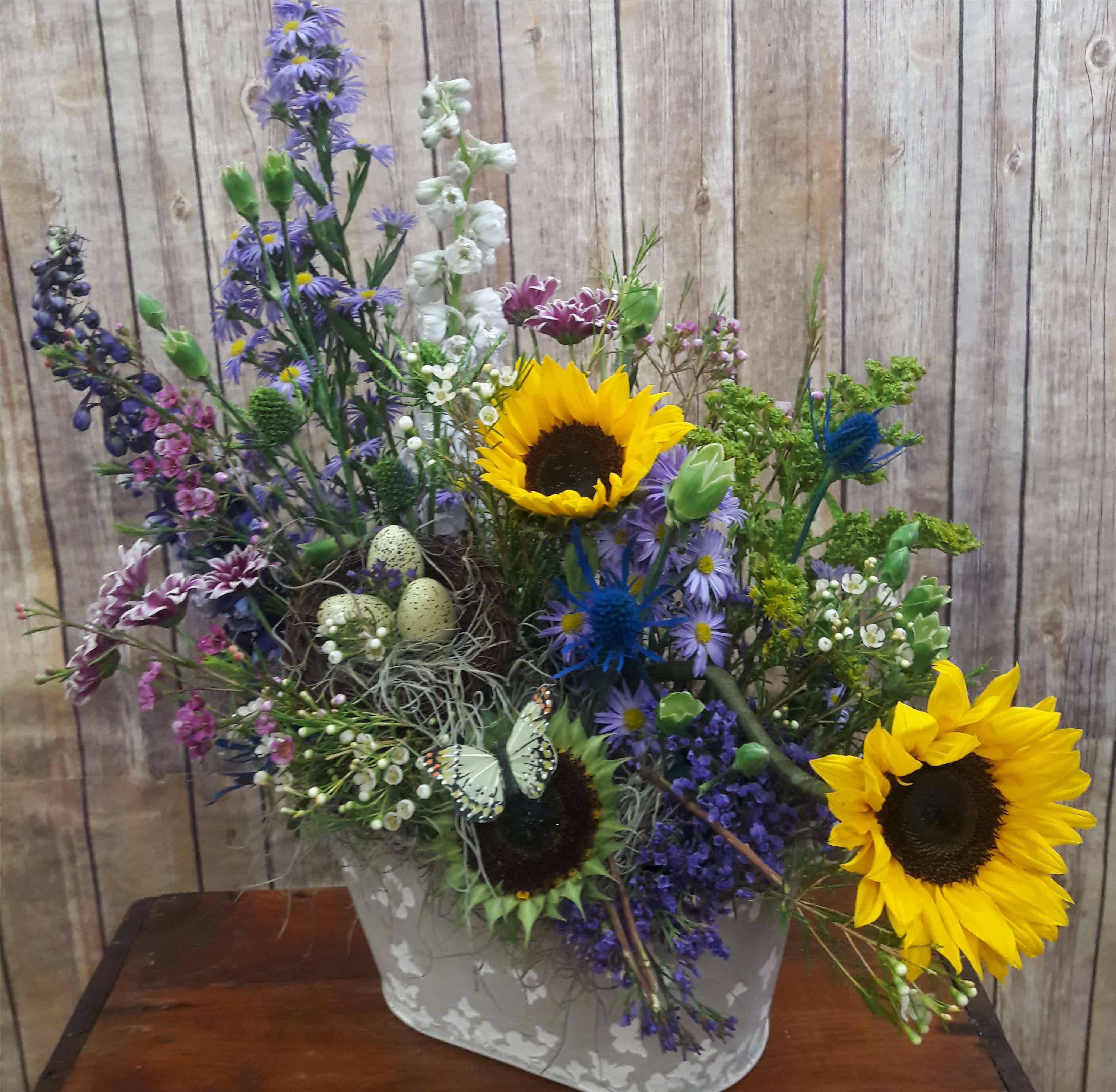 Mixed bouquet with sunflowers and purple flowers in a gray container