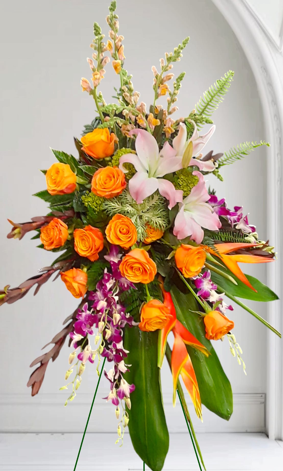 Orange roses and pink lilies with purple orchids in a tall arrangement