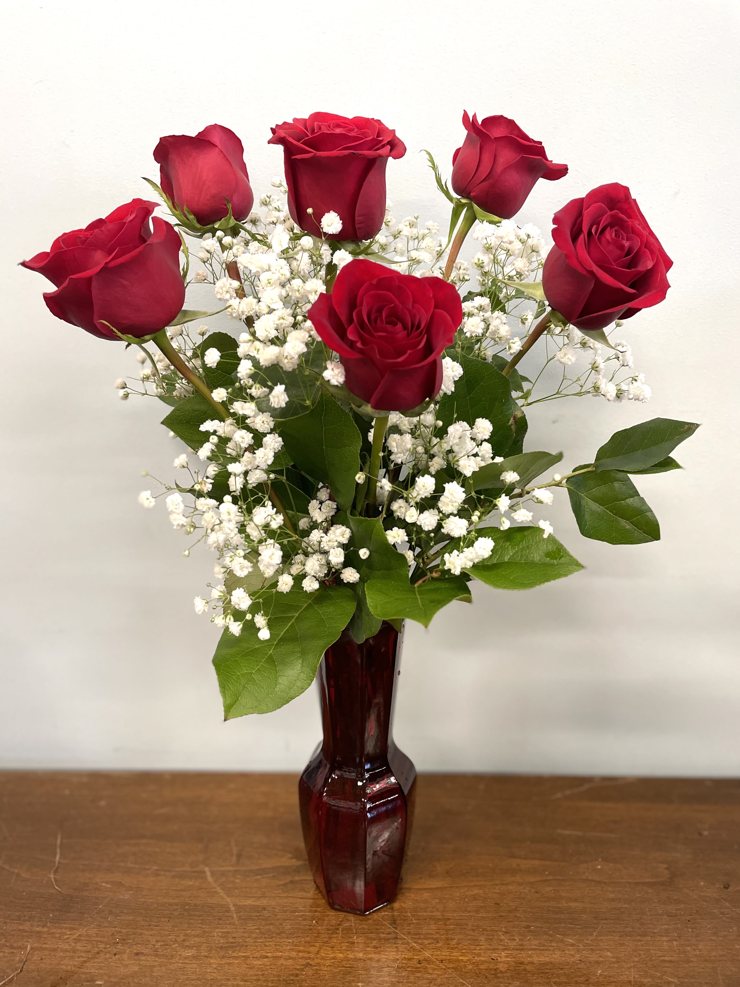 Red roses arranged in a burgundy vase with white baby's breath