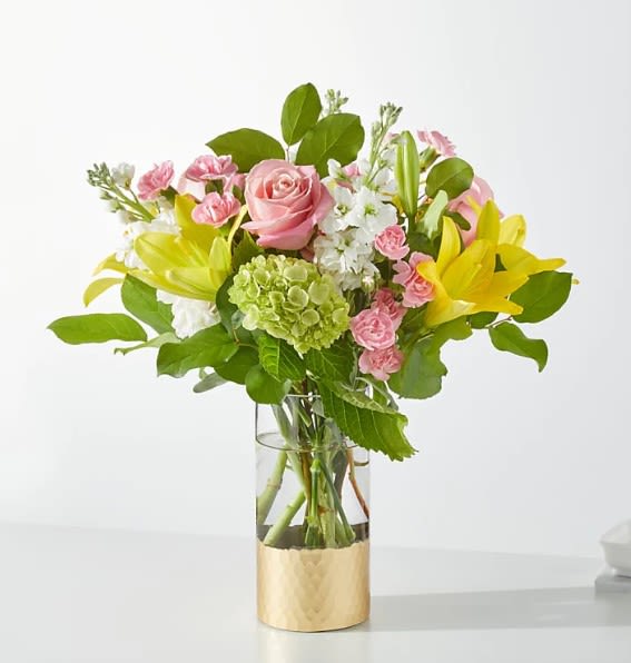 Pink roses and yellow lilies in a glass vase with a gold base