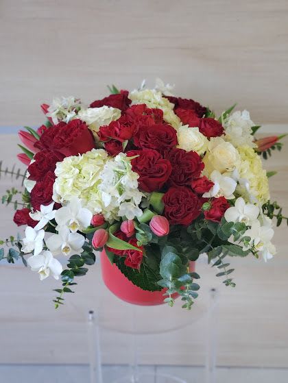 Round arrangement of red roses, white hydrangeas, orchids and pink tulips in a red hat box