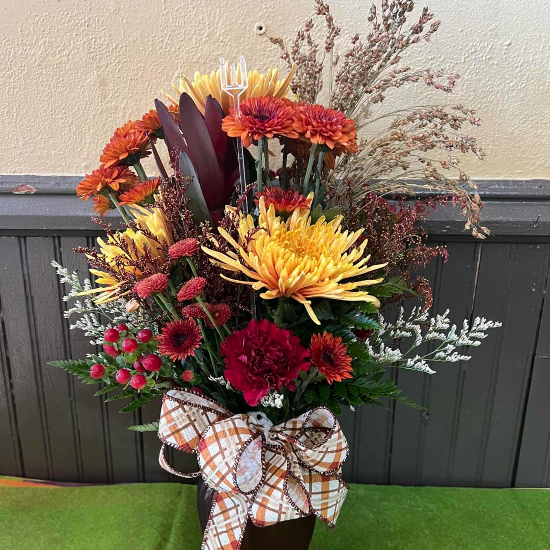 Autumn floral arrangement with yellow, orange, and red blooms in a dark vase