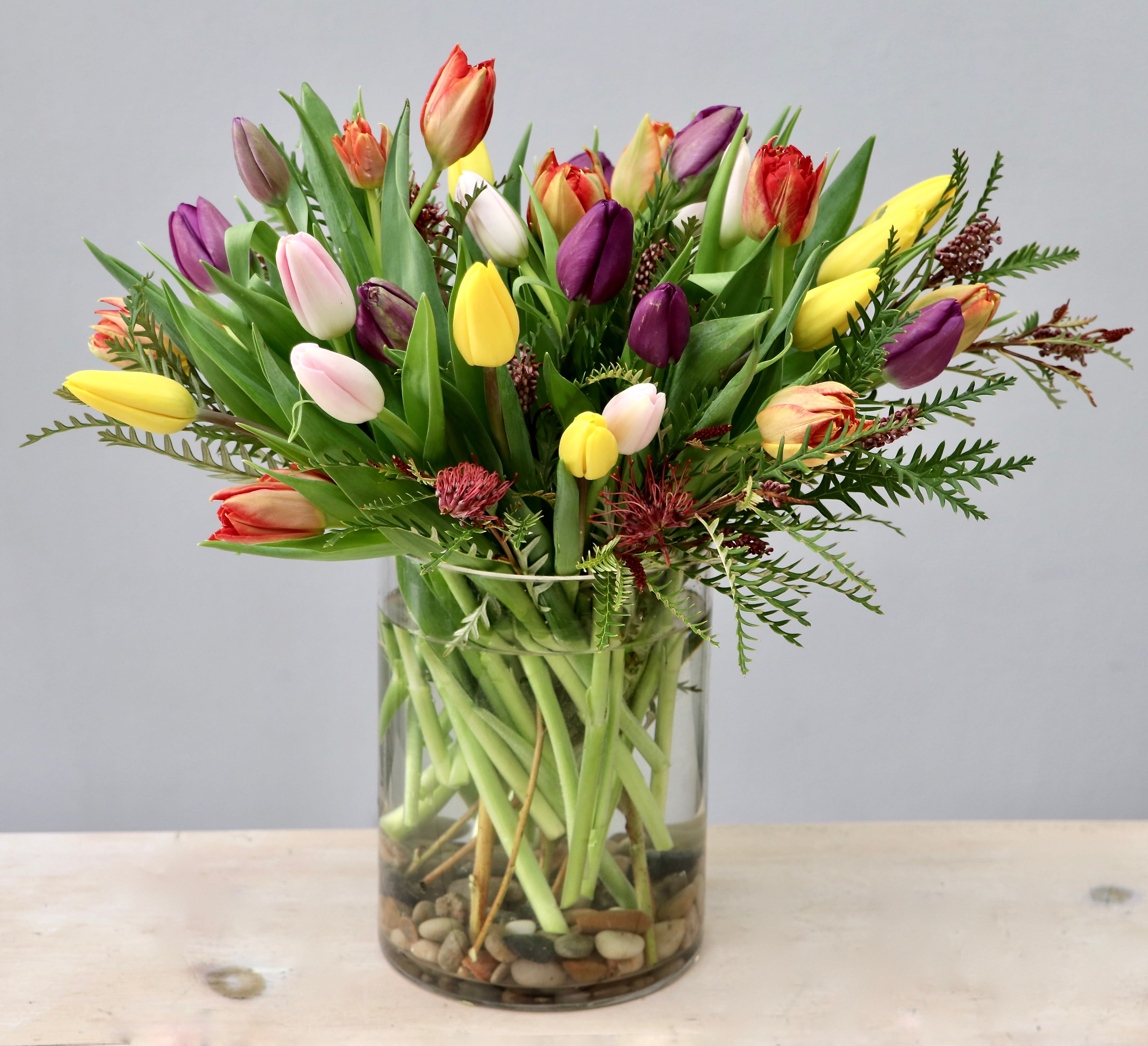 Tall clear glass vase of mixed-color tulips with river stones at the base