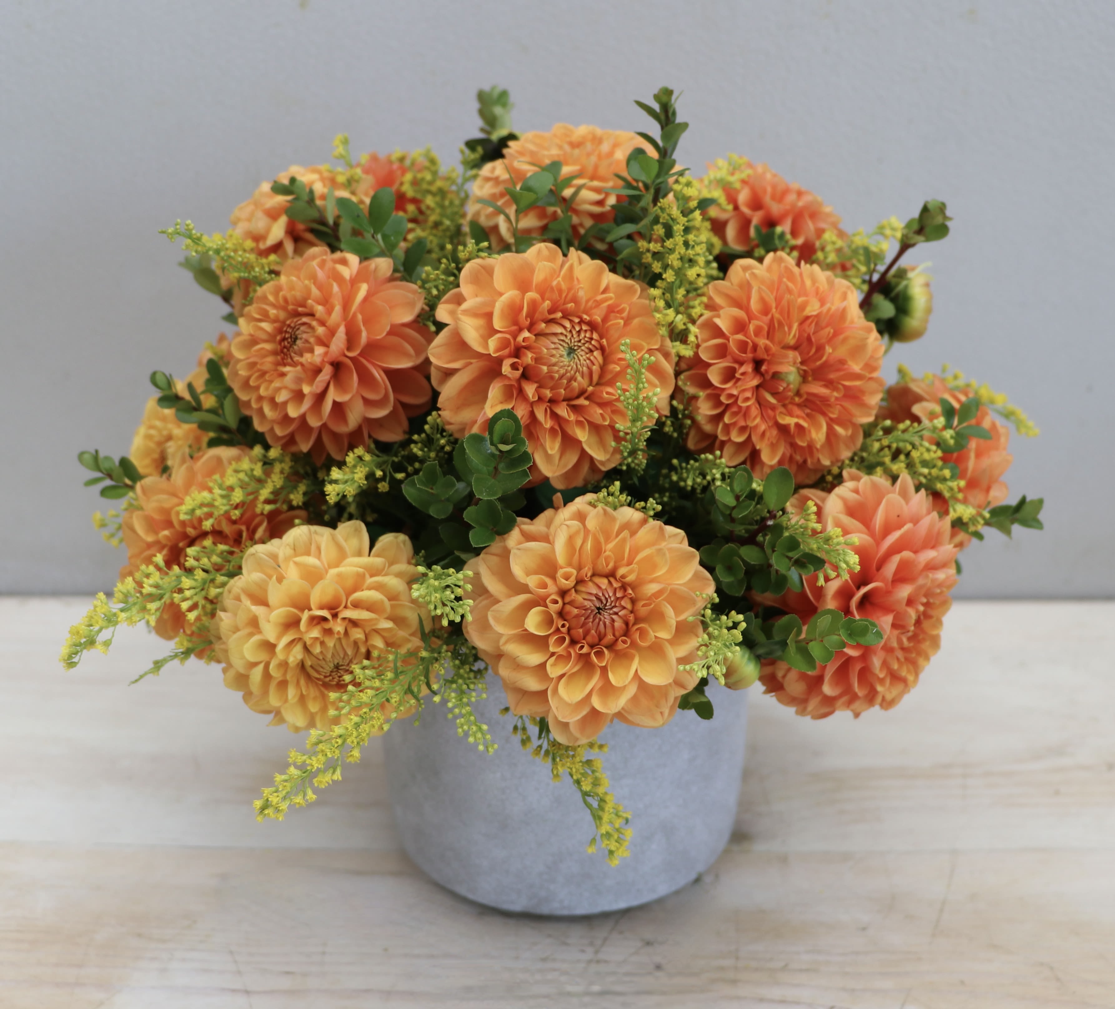Low arrangement of orange dahlias with yellow accents in a gray ceramic pot