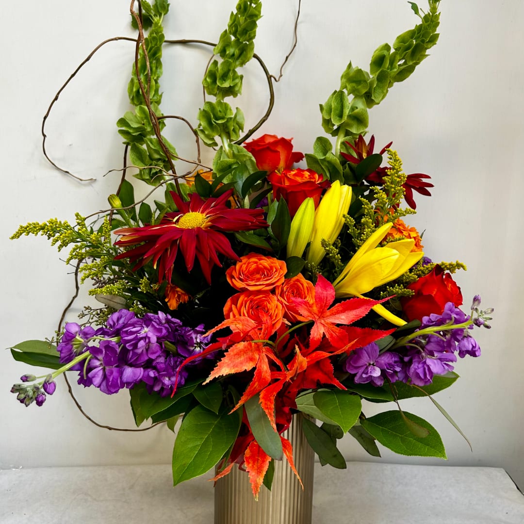 Colorful mixed bouquet in a ribbed vase with red, orange, yellow, and purple blooms