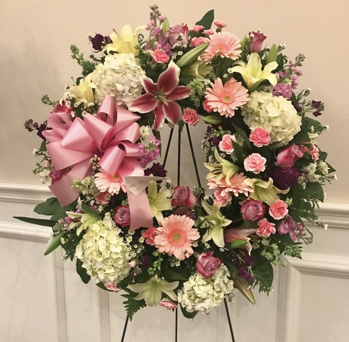 Heart-shaped floral wreath with pink ribbon and mixed pastel flowers on an easel