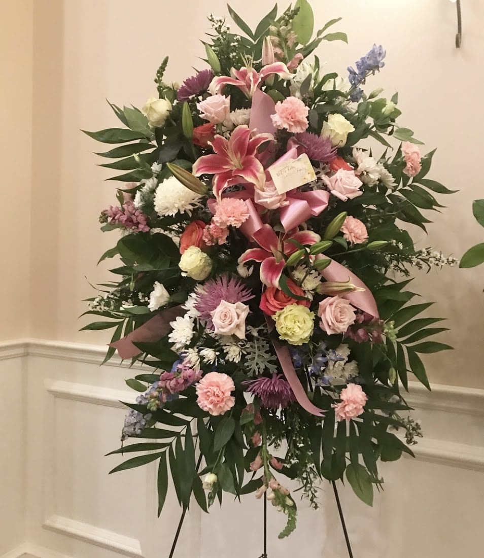 Standing floral spray with pink lilies, roses, and carnations on an easel