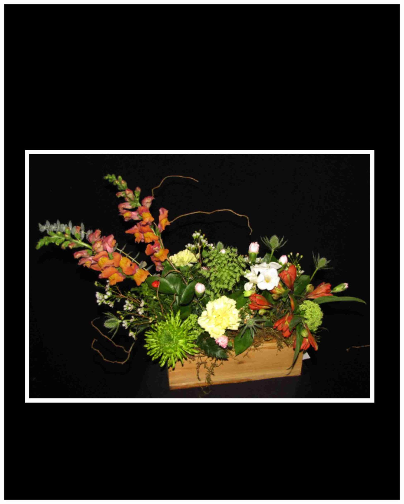 Mixed floral arrangement in a wooden box with orange, green, and white blooms