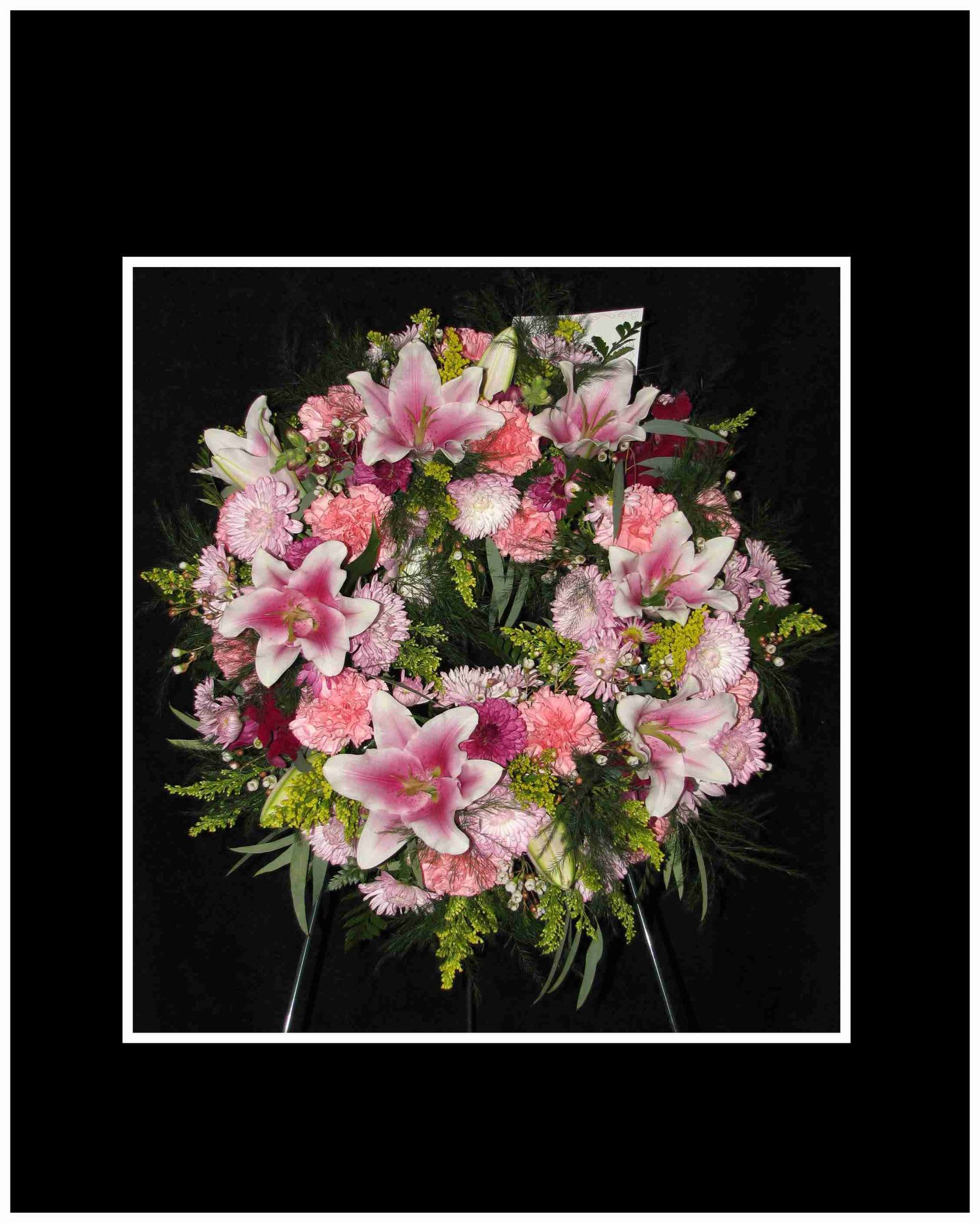 Pink lilies and carnations arranged in a wreath on a black background