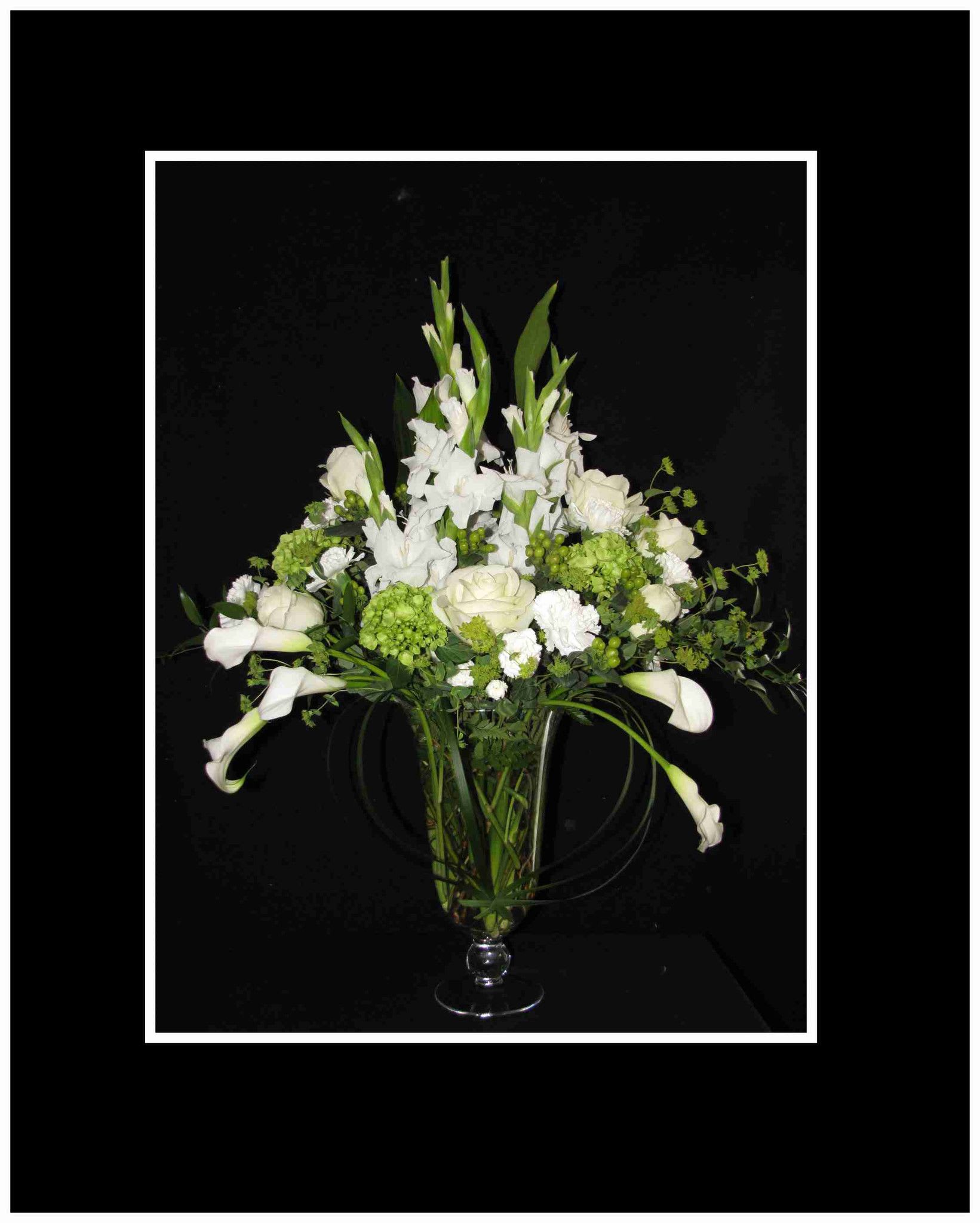 White flowers and green blooms arranged in a clear glass vase