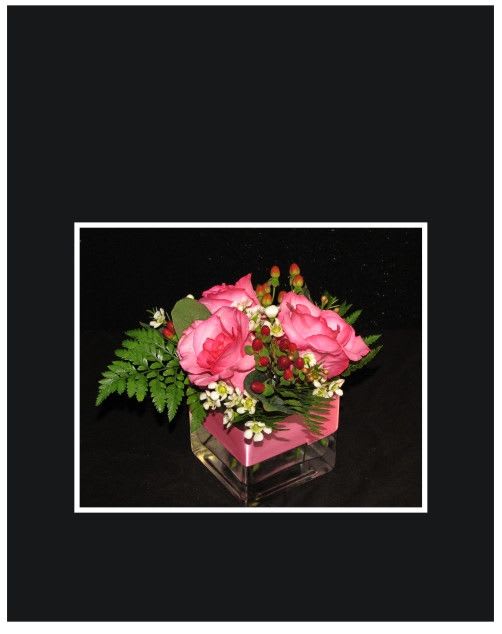 Pink roses arranged in a square glass vase with greenery