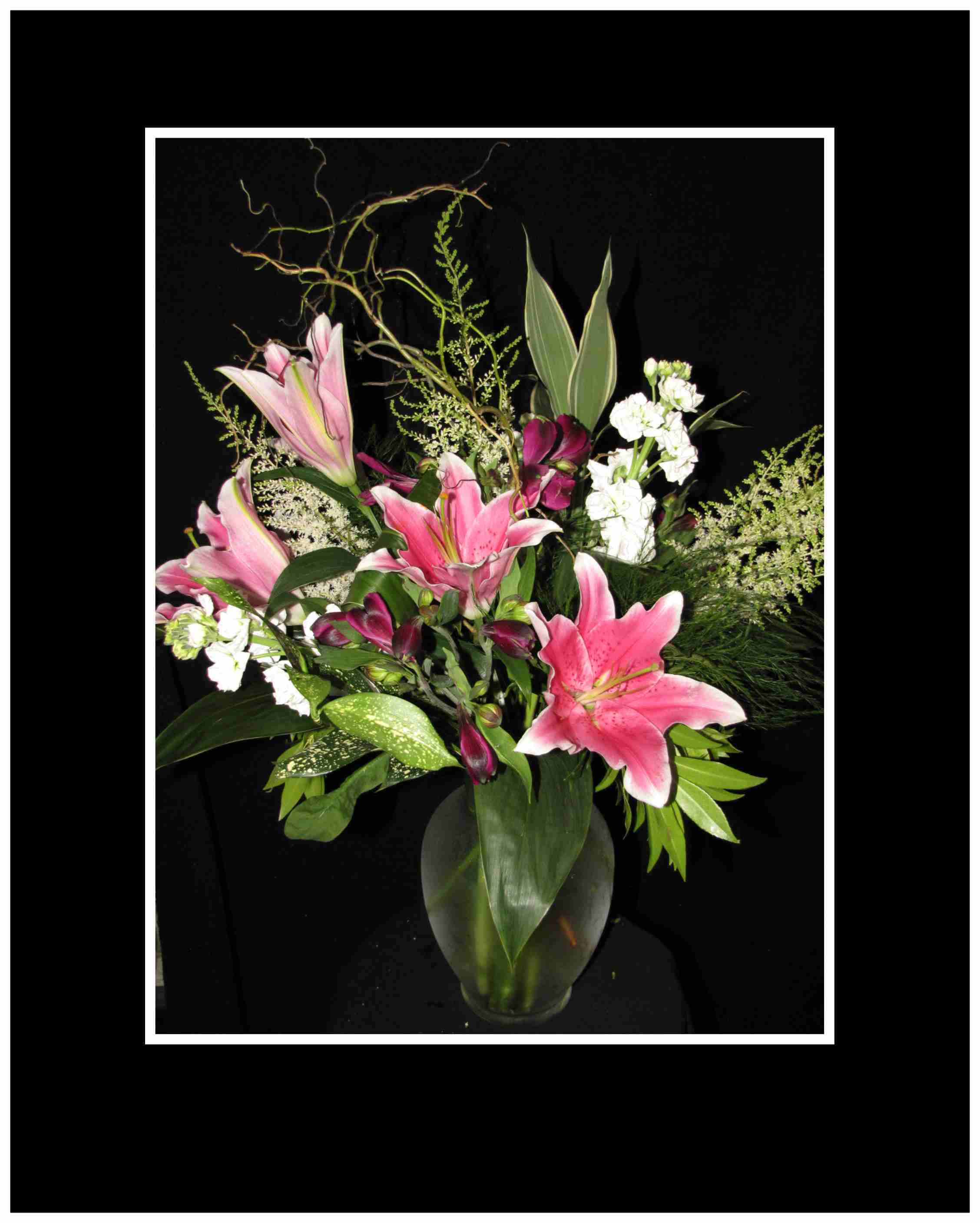 Pink lilies and white flowers arranged in a glass vase