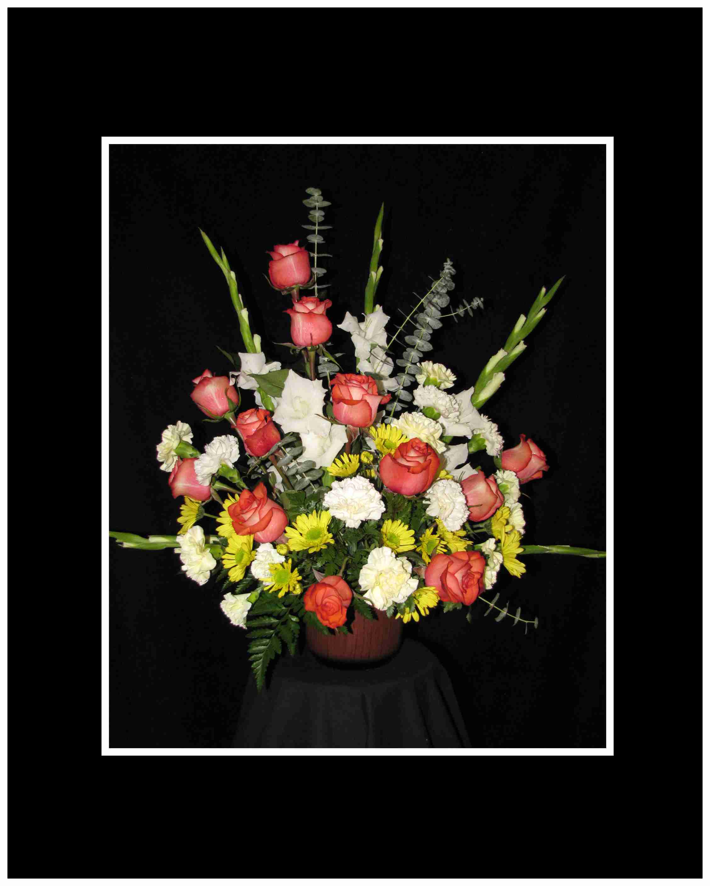 Arrangement of coral roses, white flowers, and yellow daisies in a vase
