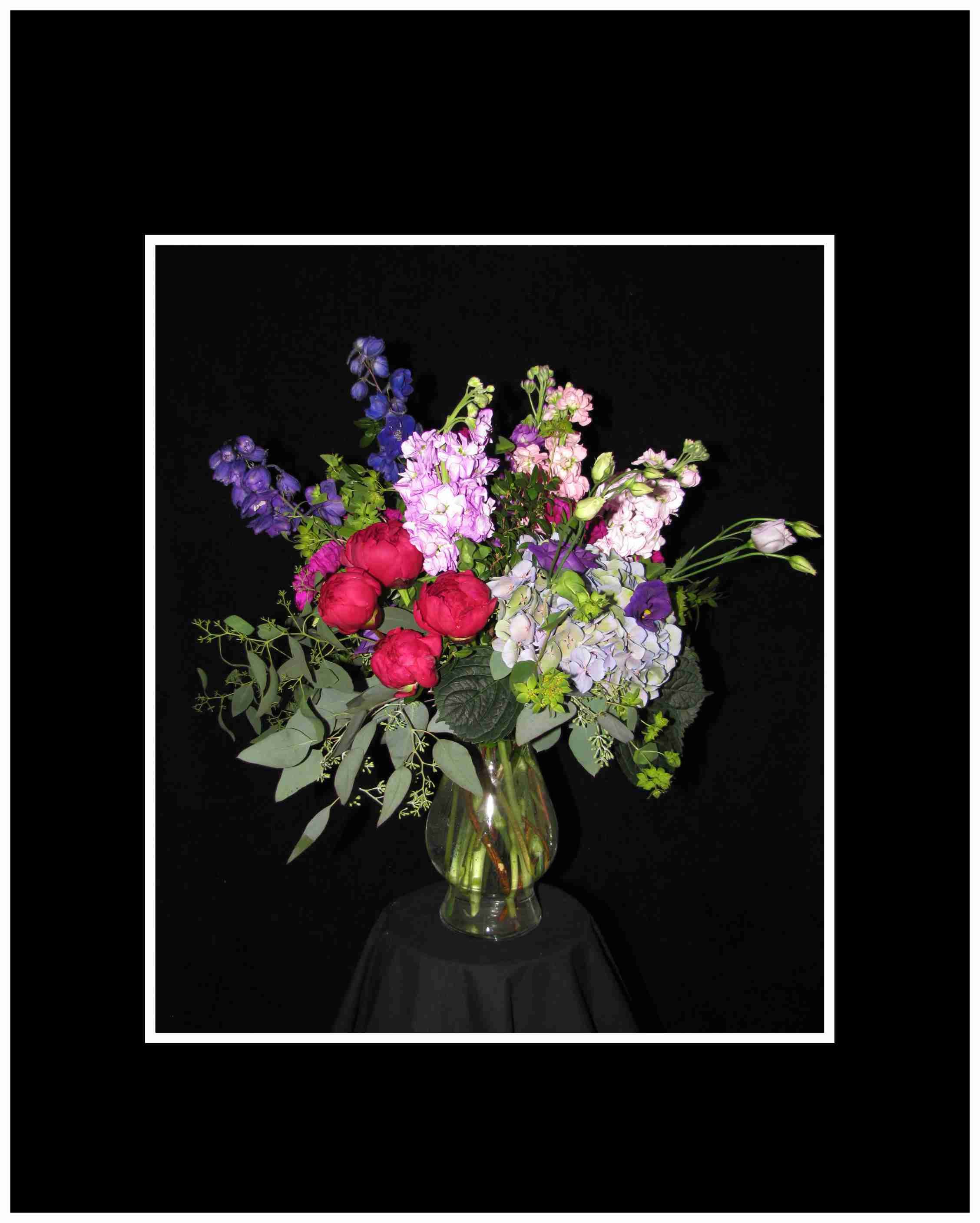 Mixed bouquet of pink, purple, and blue flowers in a clear glass vase