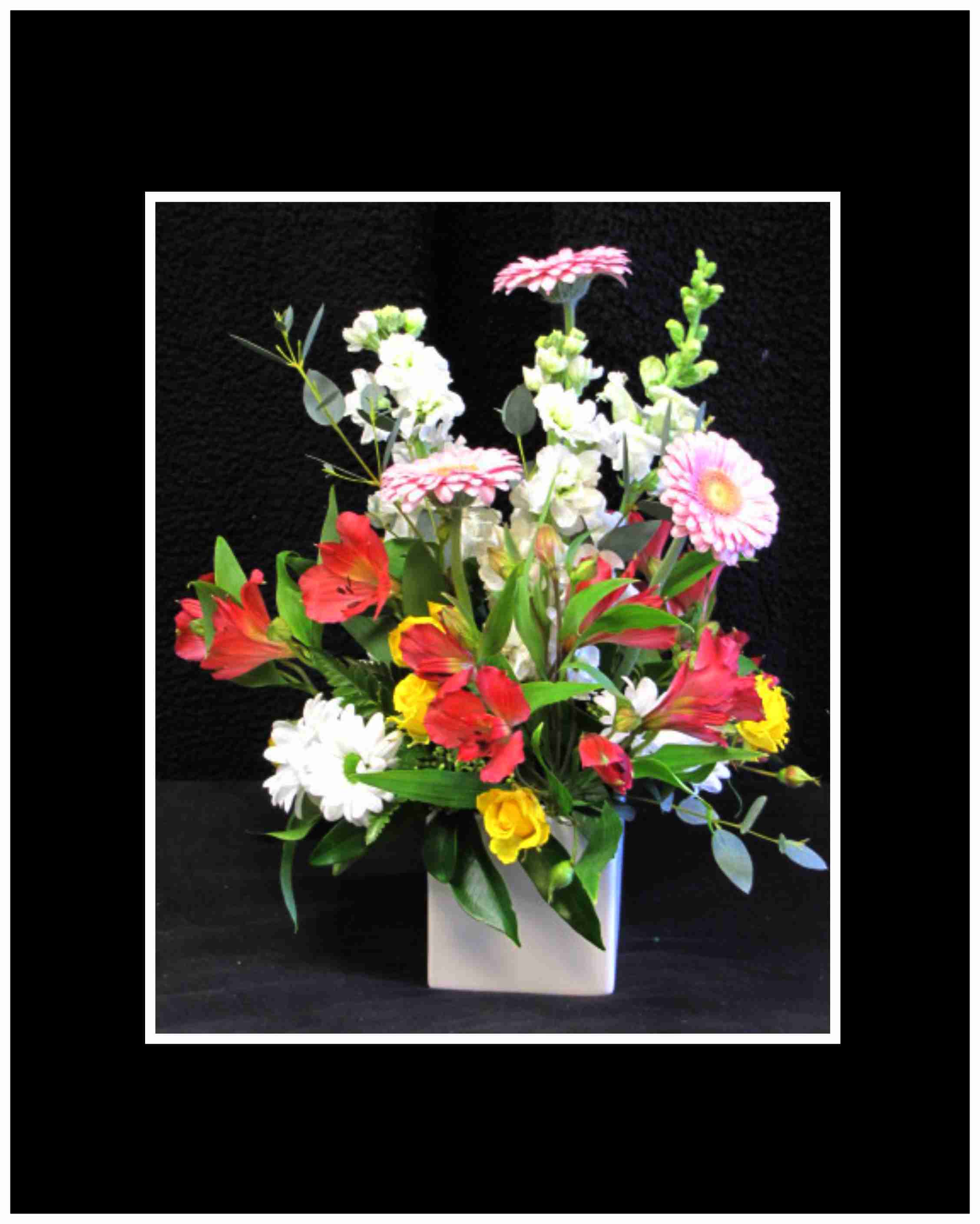 Mixed bouquet of pink, red, white, and yellow flowers in a white vase