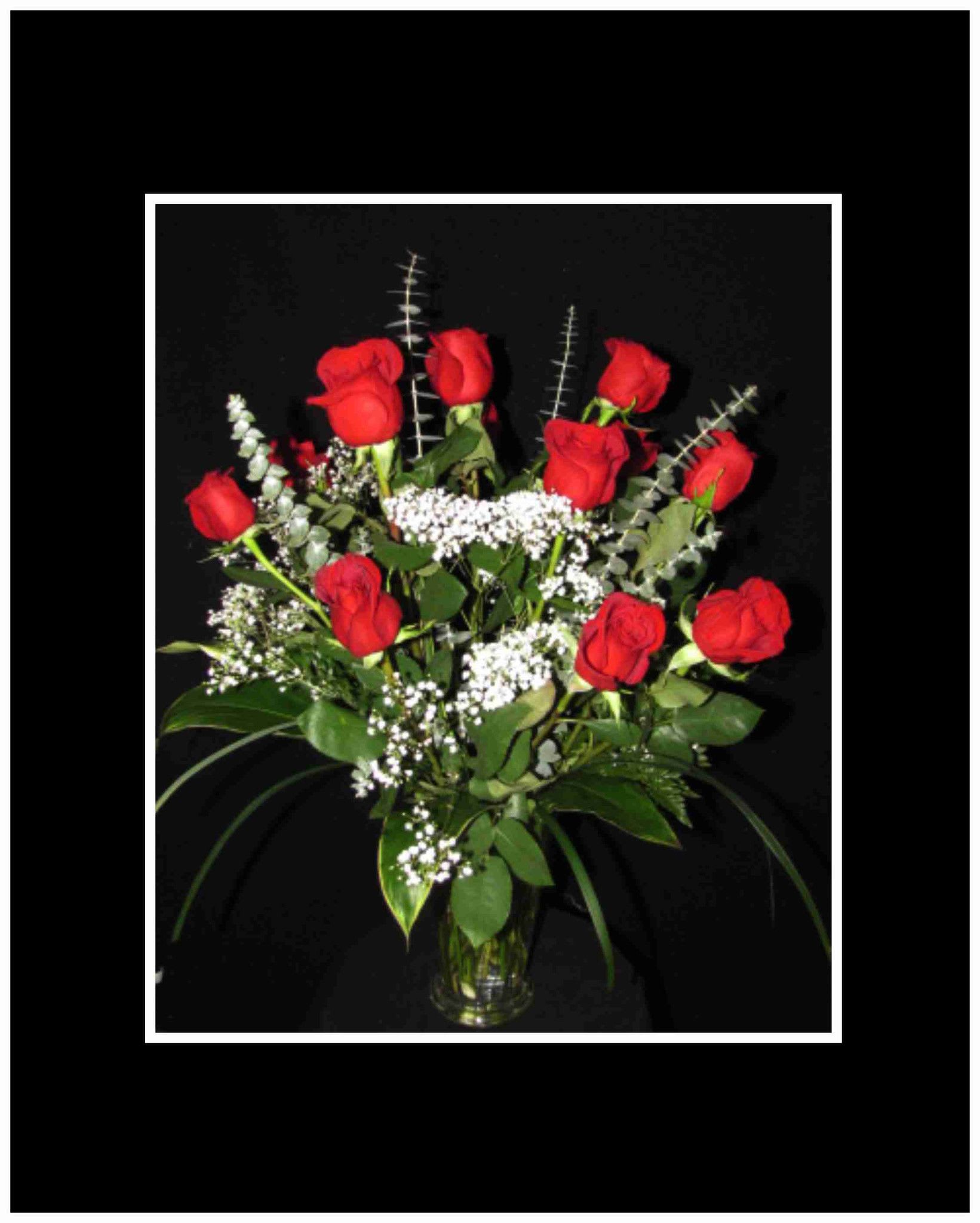 Red roses arranged in a clear glass vase with white filler flowers