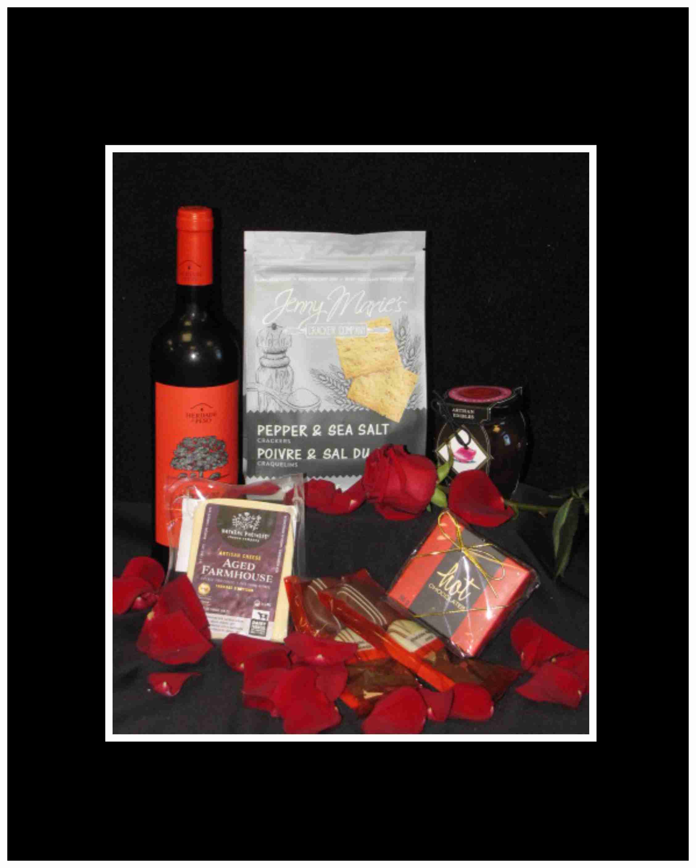 Wine bottle, crackers, chocolate, and a jar arranged with red rose petals