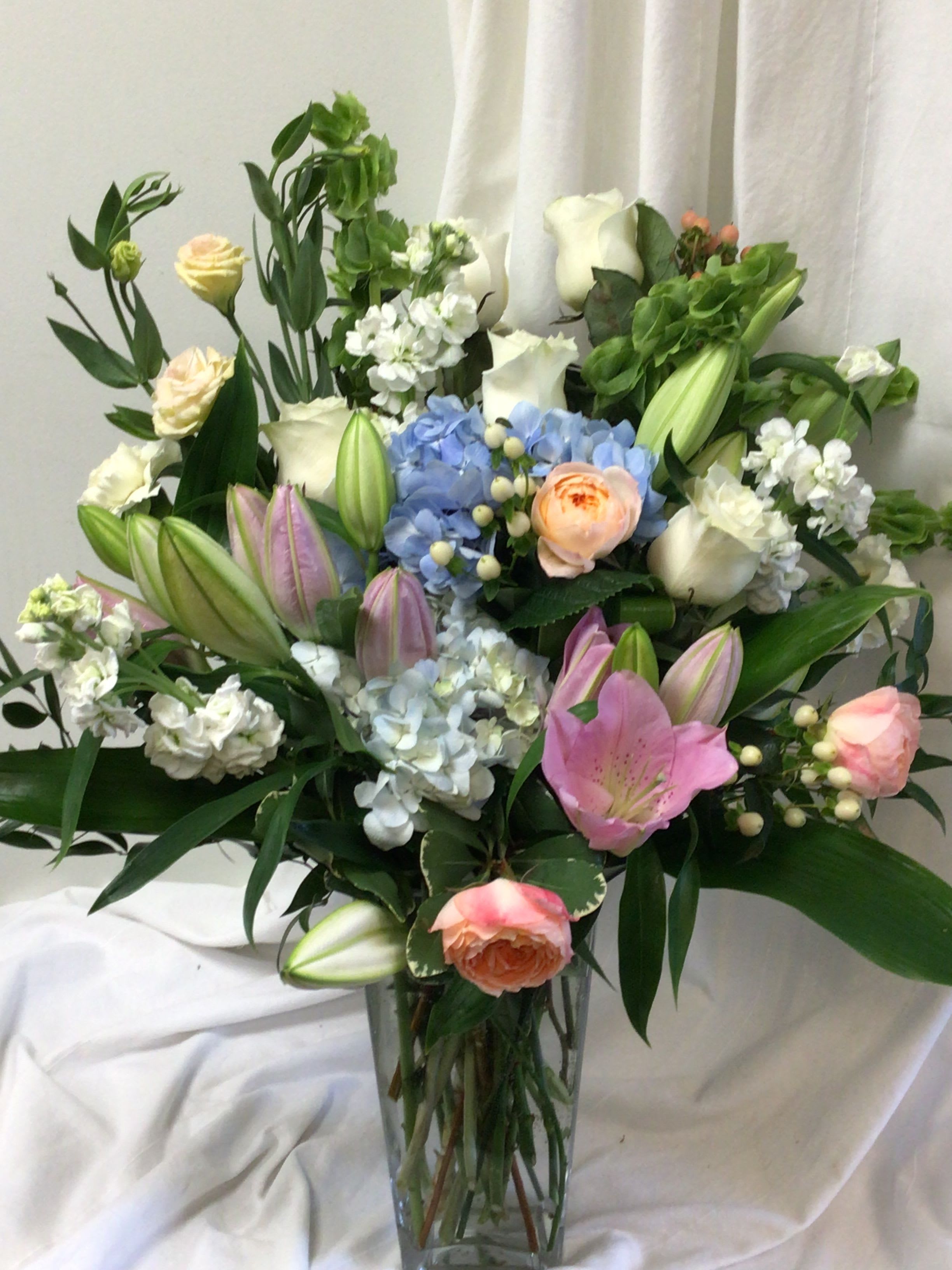 Mixed bouquet of lilies, roses, hydrangeas, and white blooms in a glass vase