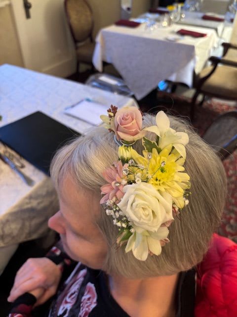 Floral hairpiece with pink, white, and yellow flowers worn in gray hair