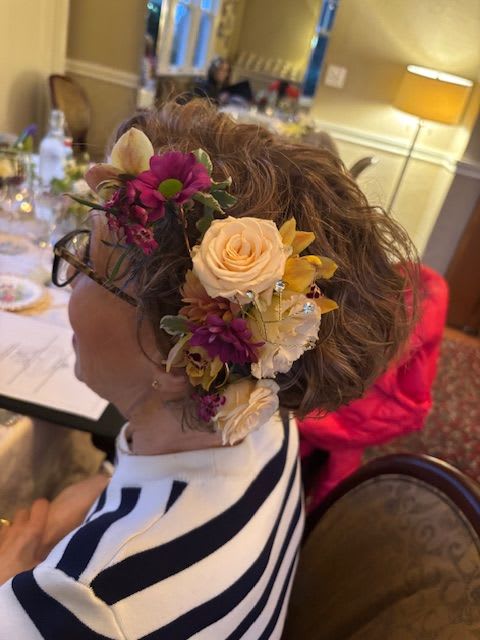 Floral hairpiece with cream roses and purple flowers worn in a woman's hair