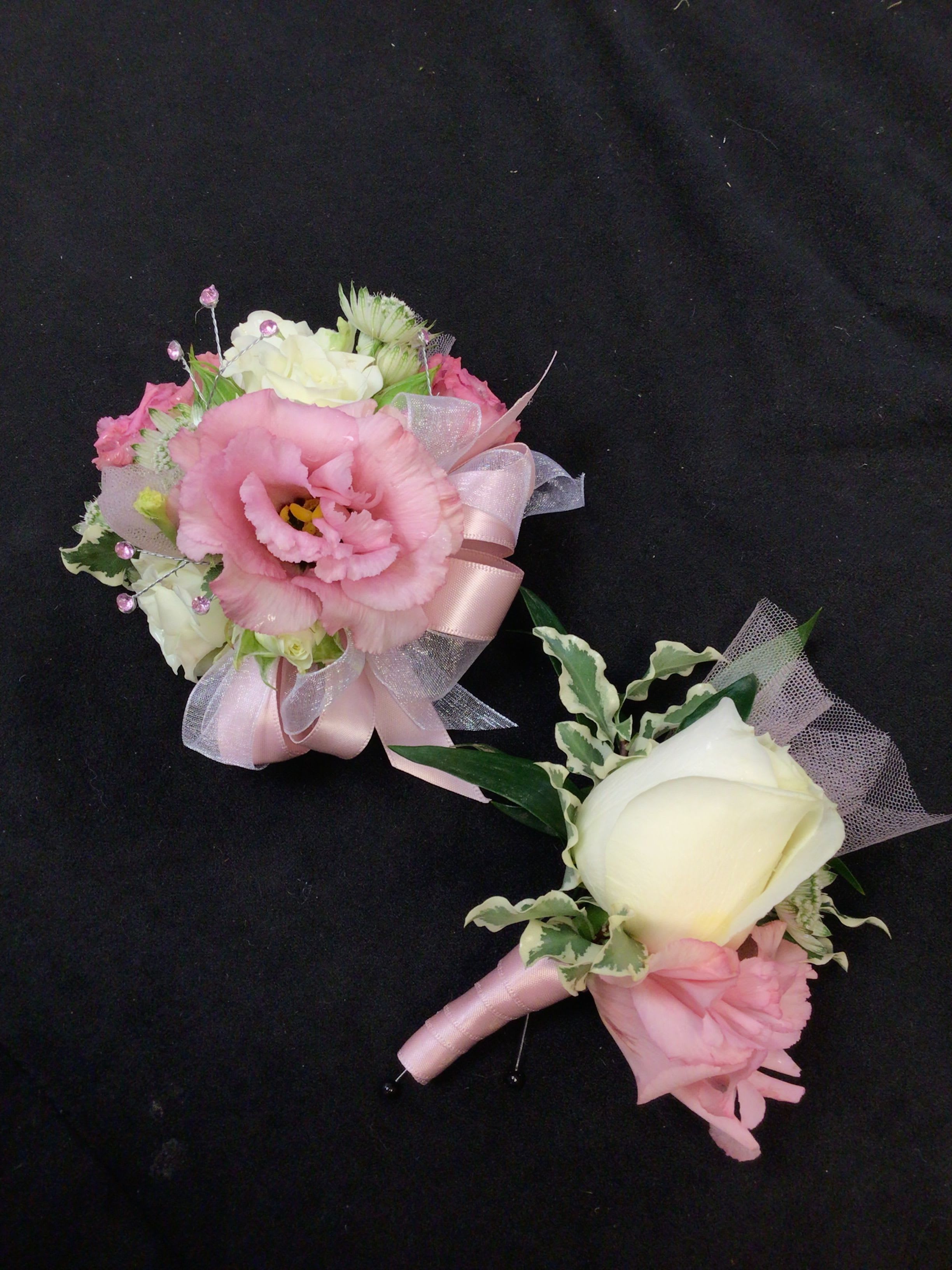 Two pink and white floral boutonnieres with ribbon accents