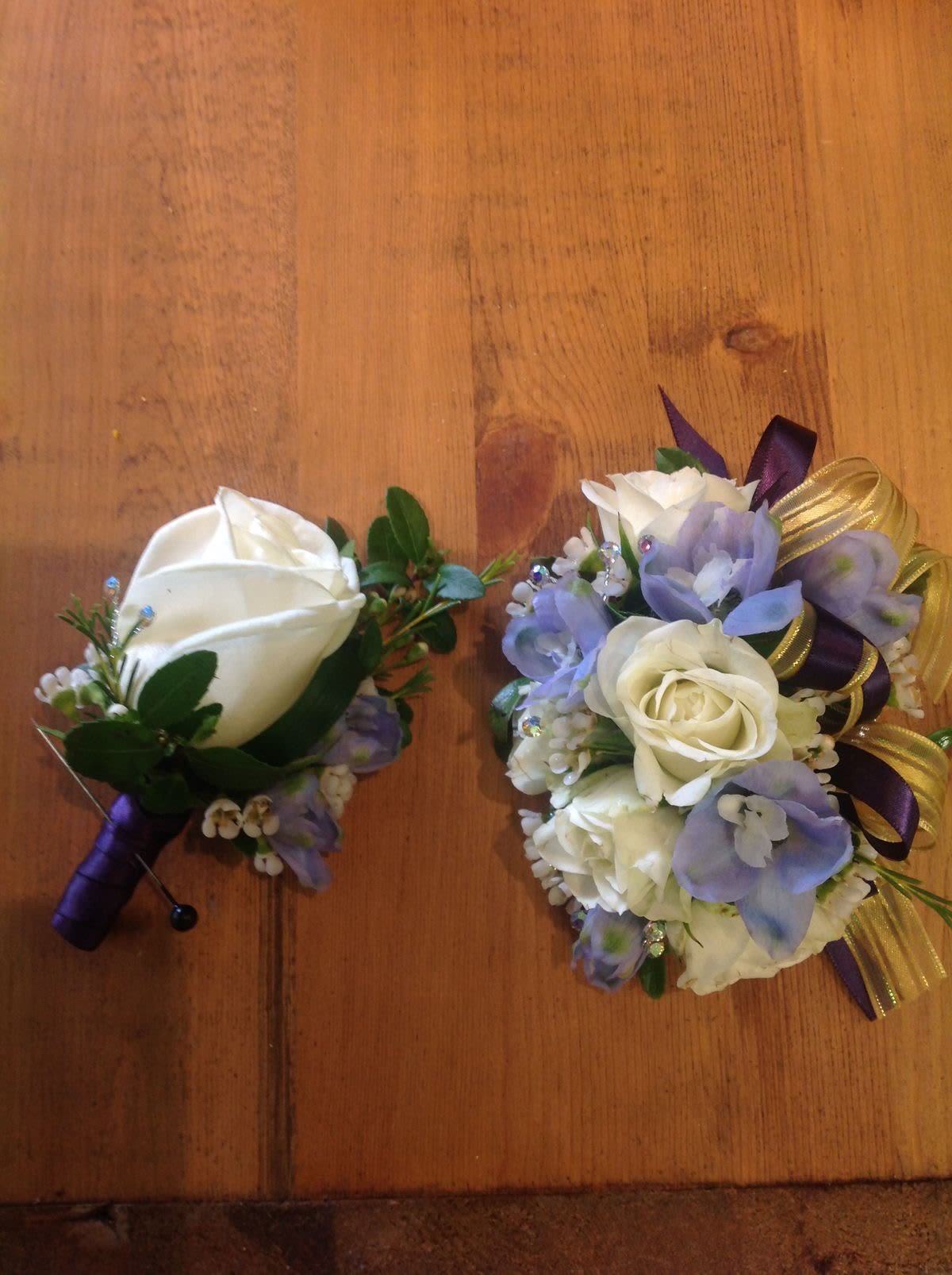 Two small floral corsages with white roses and purple accents on a wooden surface.