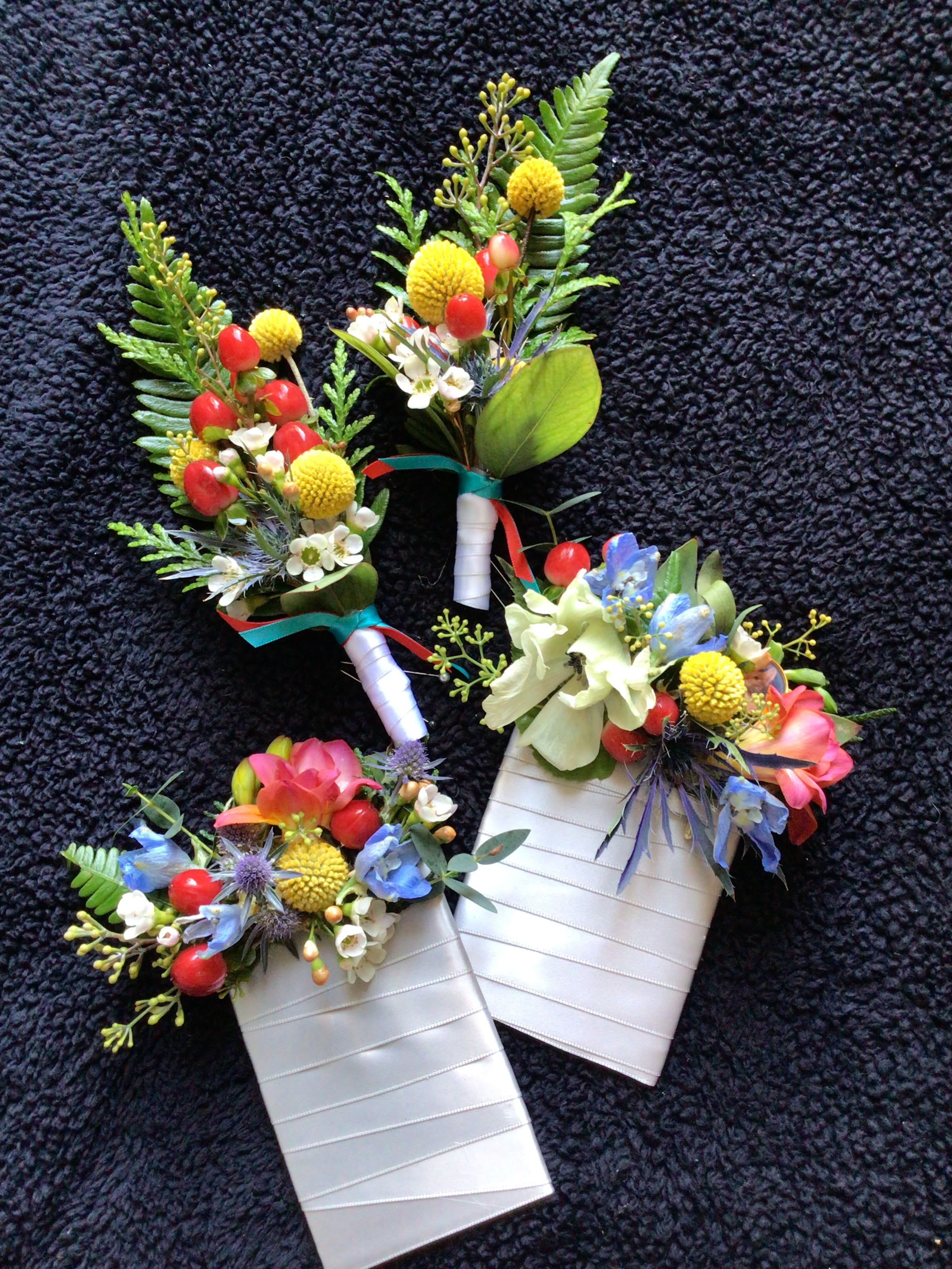 Three floral boutonnieres with colorful blooms and ribbon-wrapped stems
