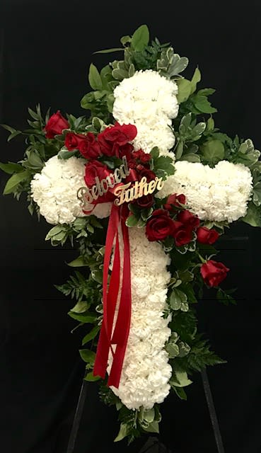 Cross-shaped floral tribute with white blooms and red roses on a black stand