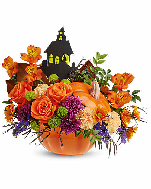 Orange floral arrangement in a pumpkin container with a haunted house pick