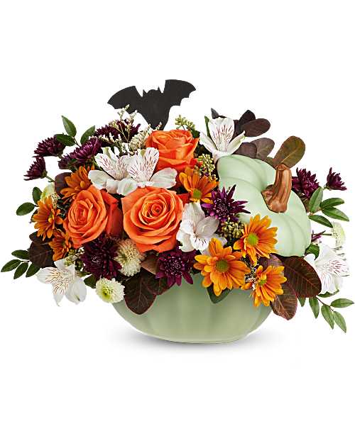 Orange roses and mixed fall flowers in a pale green pumpkin container with a bat pick
