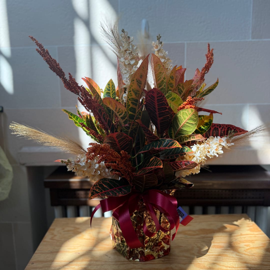 Autumn floral arrangement with multicolored leaves and cream blossoms in a wrapped container