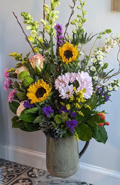 Mixed bouquet with sunflowers, daisies, and roses in a tall vase