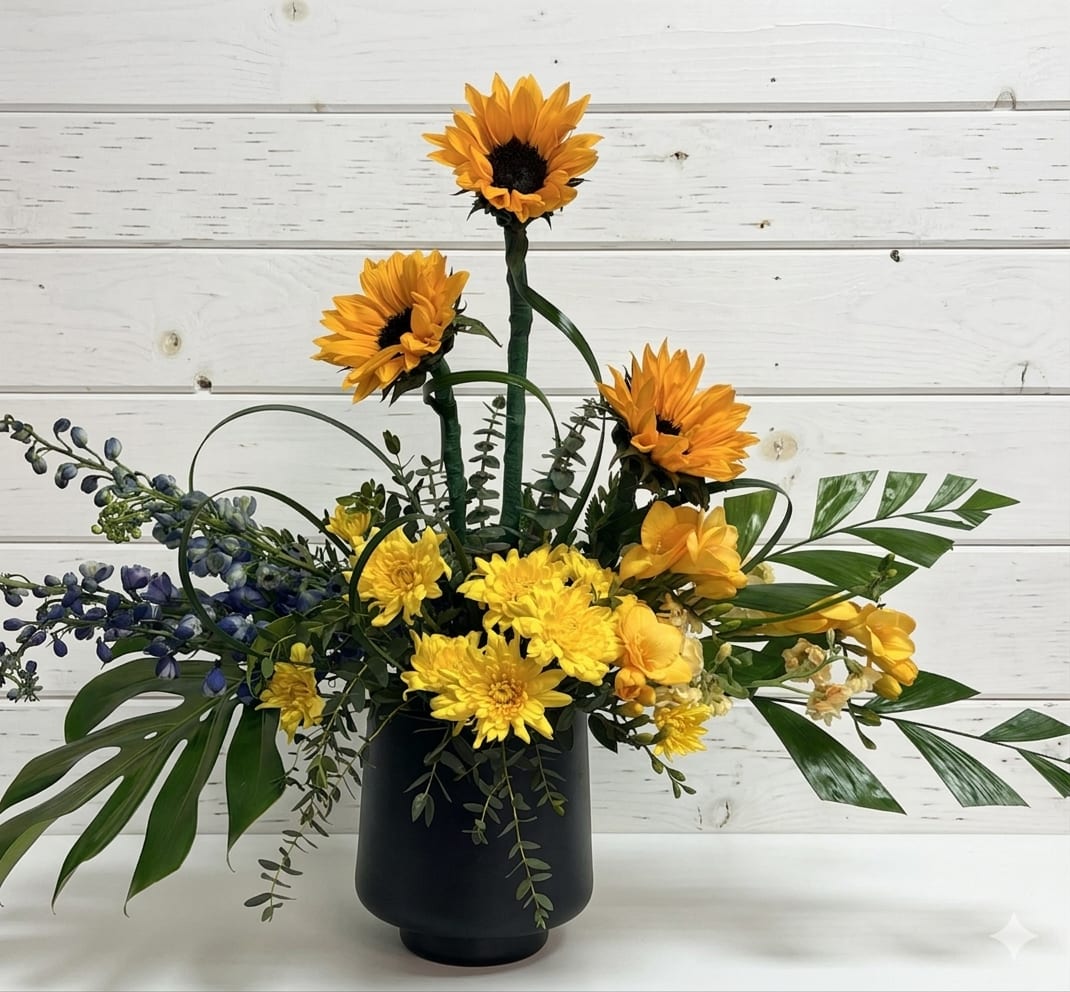 Dancing Sunflowers - Bring a burst of sunshine indoors with this cheerful garden-inspired arrangement. Featuring radiant golden sunflowers paired with soft yellow blooms and textured greenery. Perfect for birthdays, get well wishes or simply brightening someone's day.