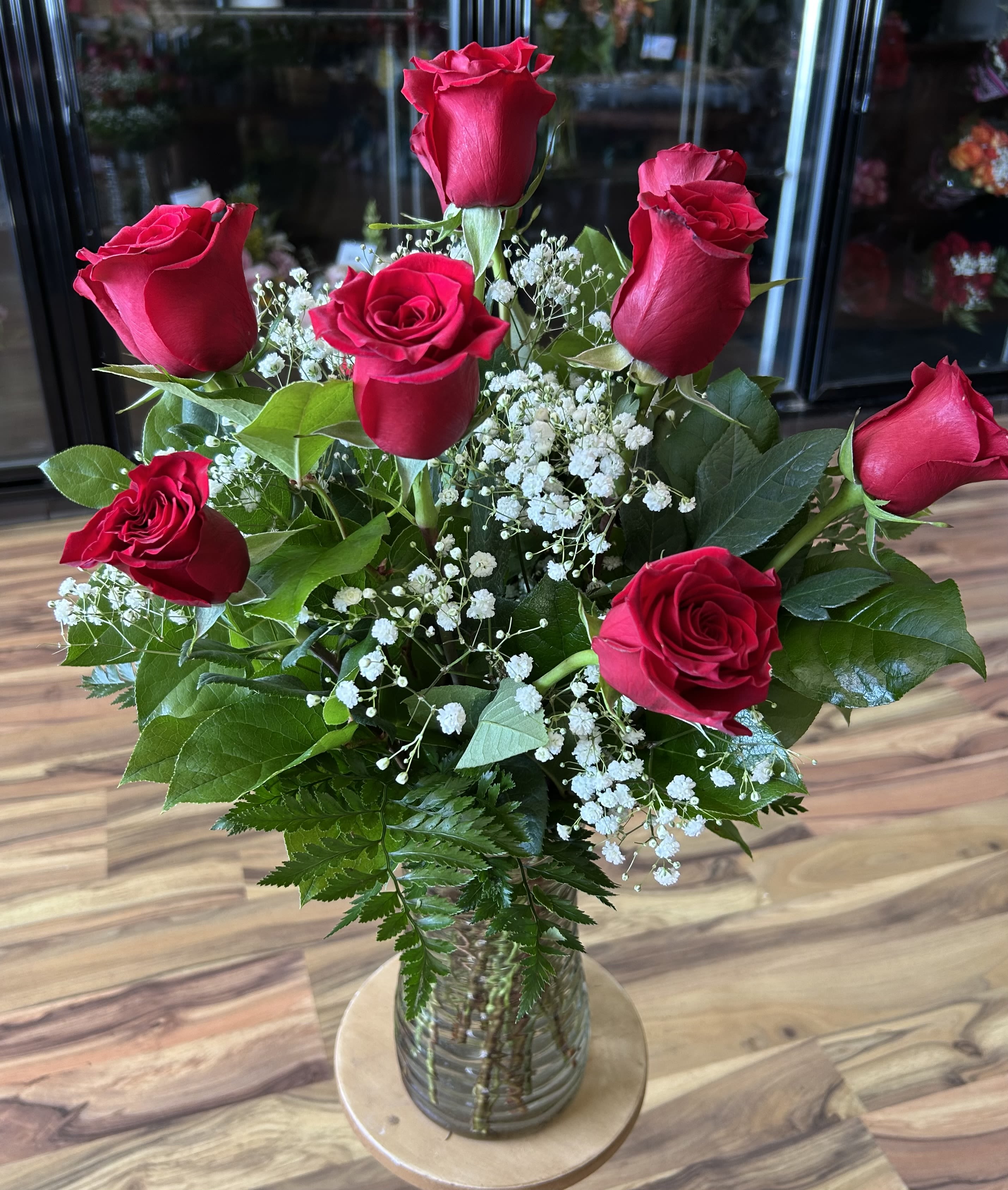 Love is in the Air - Who doesn't love a classic favorite? - 1 dozen red roses with Baby's Breath in a clear vase.  Want a different color? Please be sure and specify in the details of your order or call us at the store to let us know your preference.  