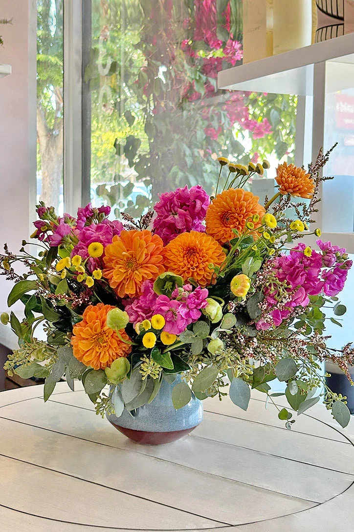 Bright mixed flower arrangement in a blue vase with orange and pink blooms