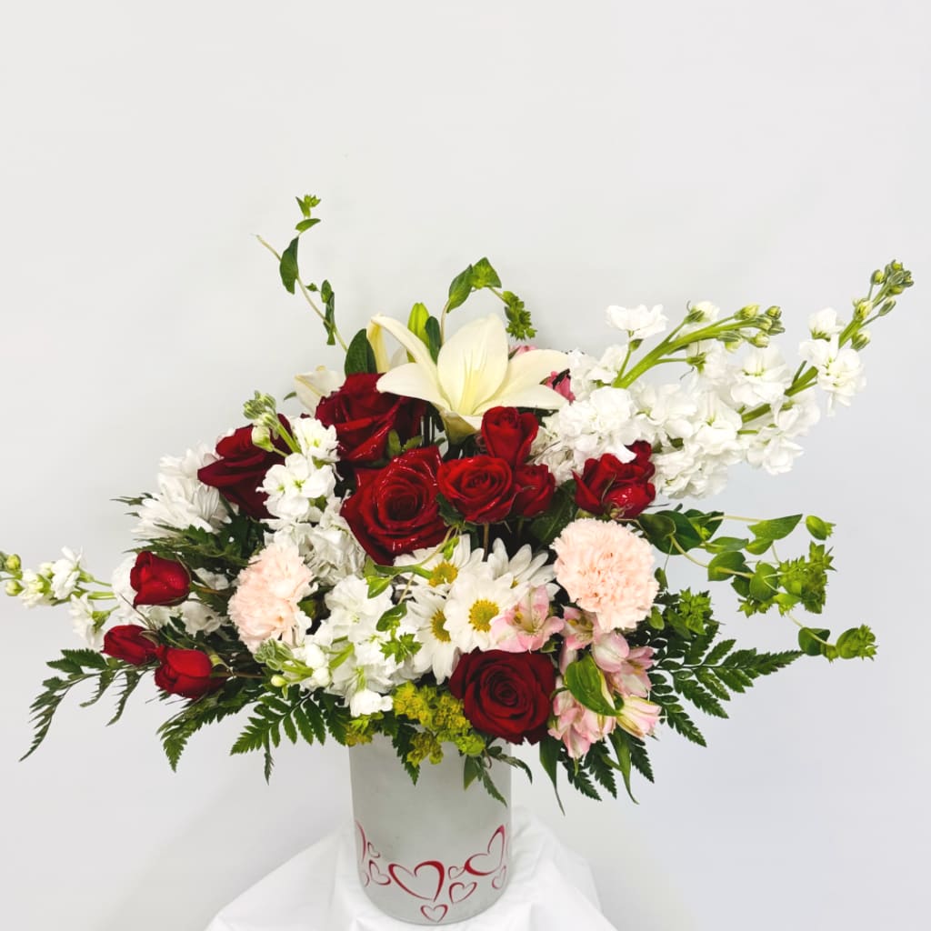 Red roses and white lilies in a white vase with mixed blooms