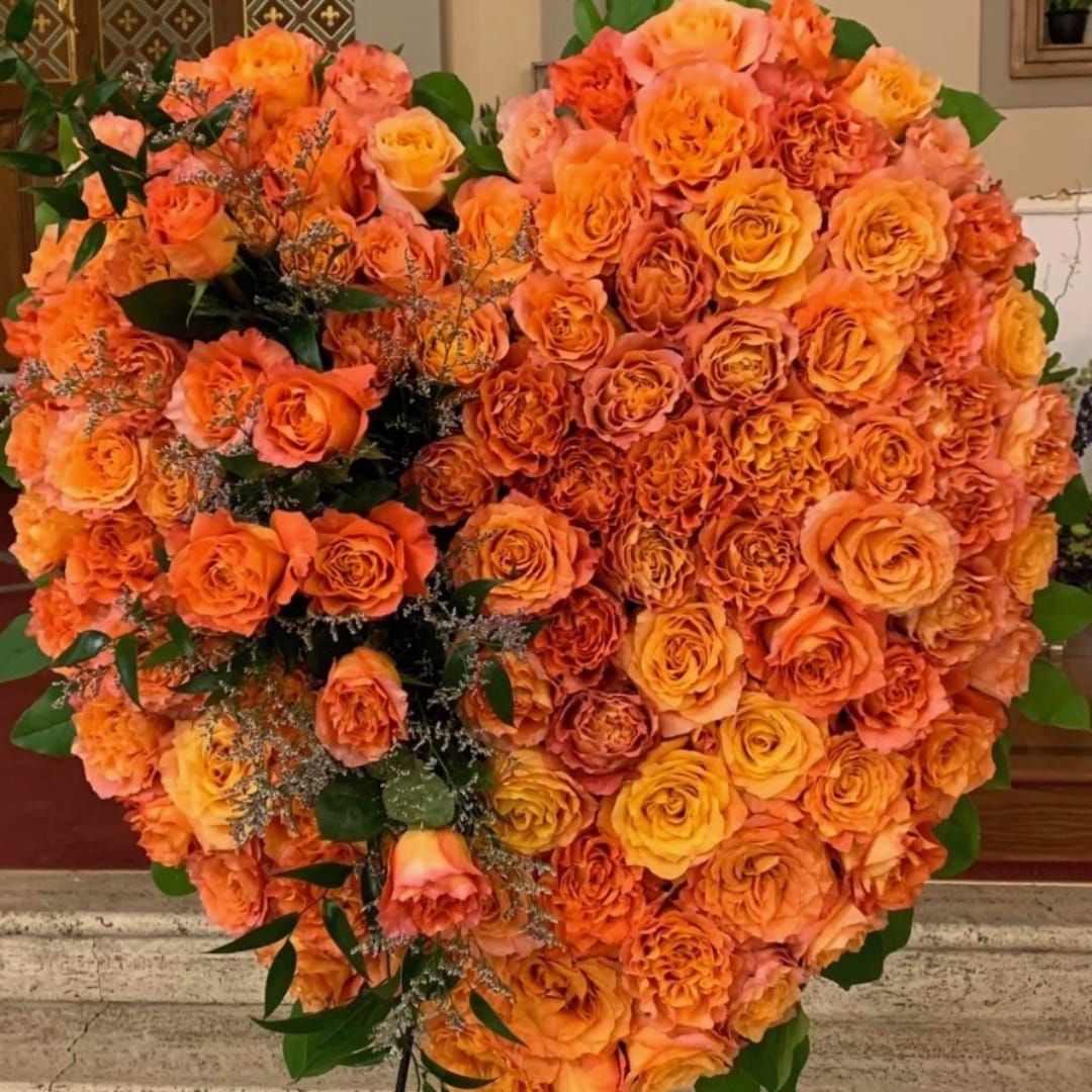 Large heart-shaped orange rose arrangement with green foliage