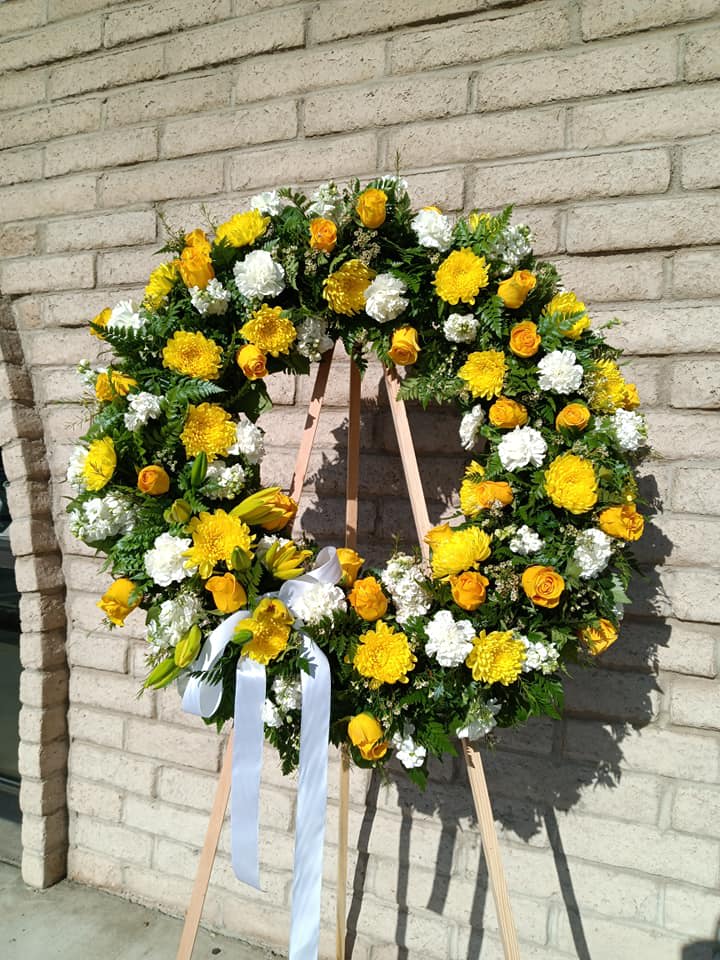 Yellow and white floral wreath on a wooden easel with a white ribbon