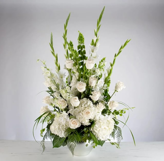 Sweet Comfort by BloomNation™ - An all white tribute, this funeral basket is pure and tranquil. Featuring a variety of white flowers and greenery, this design reaches for the sky and evokes a feeling of peace upward and outward. 
