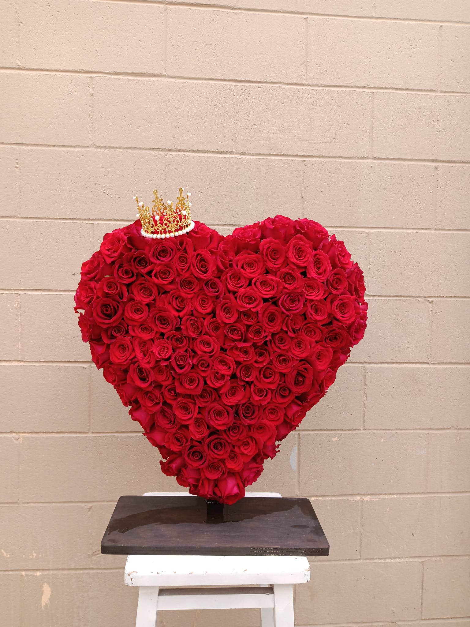 Heart-shaped arrangement of red roses with a small crown topper
