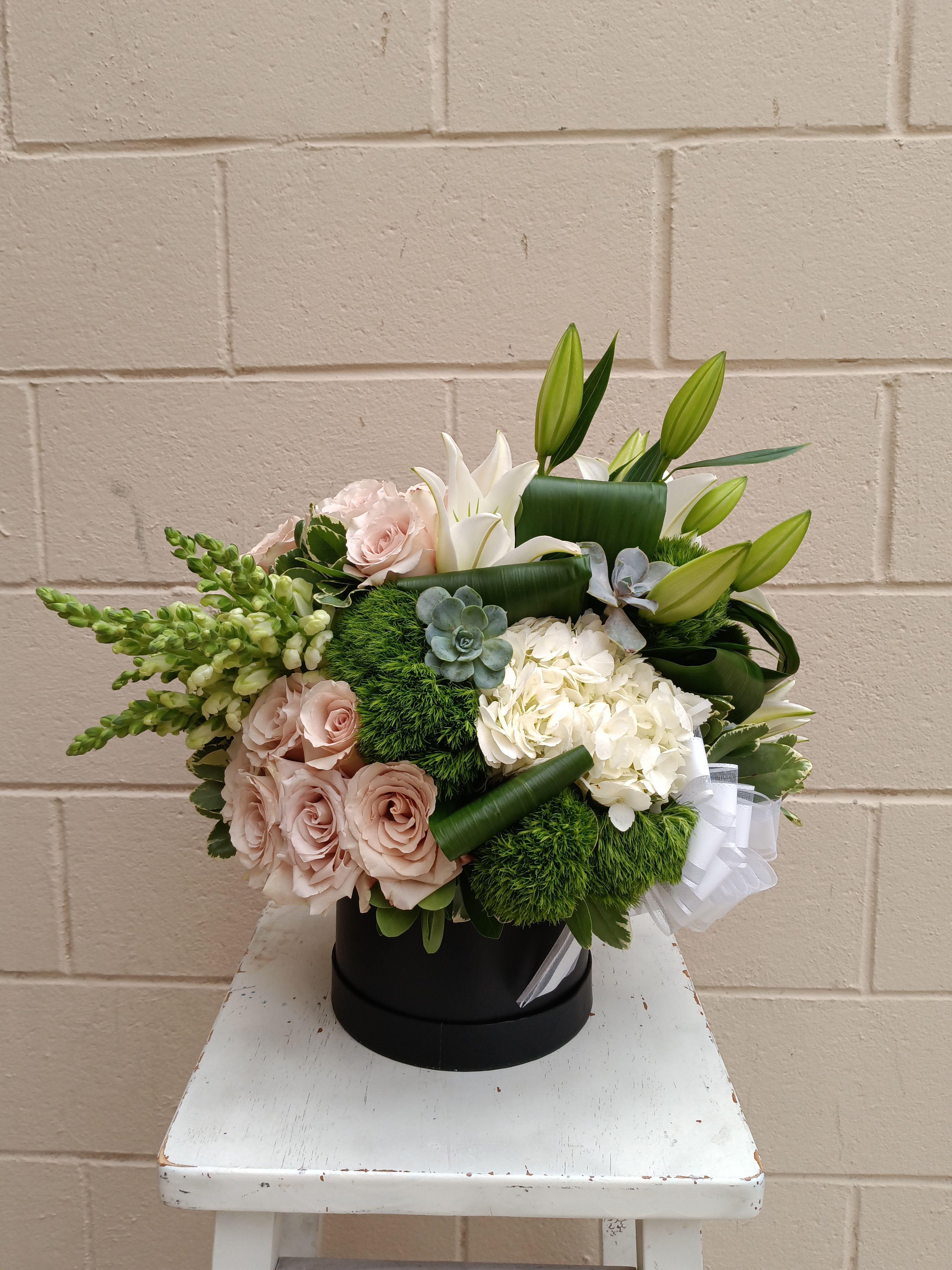 Bouquet of pale pink roses, white lilies, and hydrangeas in a black hatbox