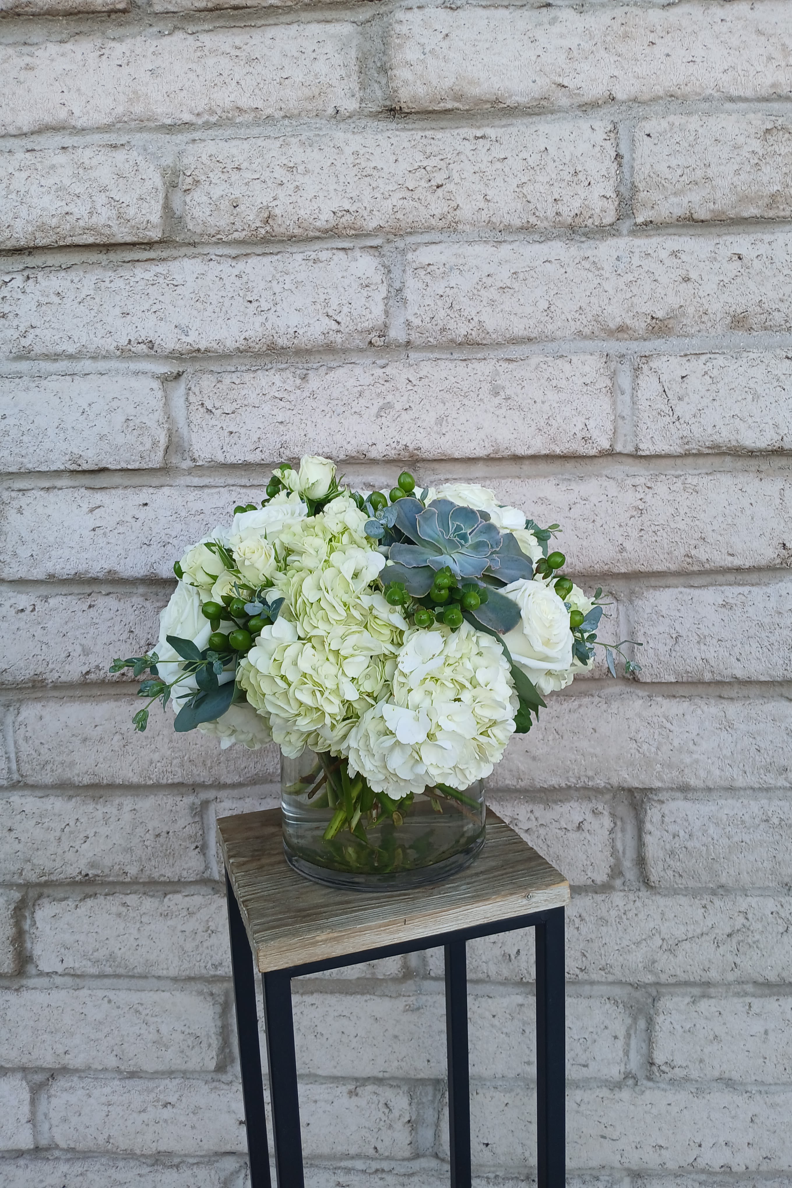 White floral arrangement in a glass vase with green accents