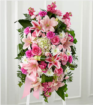 The Gently Into the Ever-After Standing Spray - Bright, fresh, beautiful and just right for an elegant expression of heartfelt sorrow and devastating loss. This classic standing arrangement is constructed by a local artisan florist of hand-selected pink blossoms ranging from pale pastels to deep blushing pink. It includes roses, carnations, stock, cushion pompons, Asiatic and Stargazer lilies and hydrangea beautifully set among a field of lush contrasting greens like aspidistra and ivy vines. It comes with a wooden easel for flexible display options and makes an impressive memorable tribute at a wake, funeral or graveside service. Your purchase includes a complimentary personalized gift message.