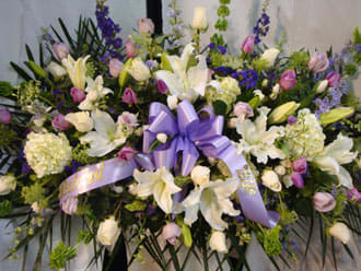 Large floral spray with white lilies, purple flowers, and a lavender ribbon