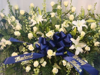White floral funeral spray with blue ribbons and a central bow