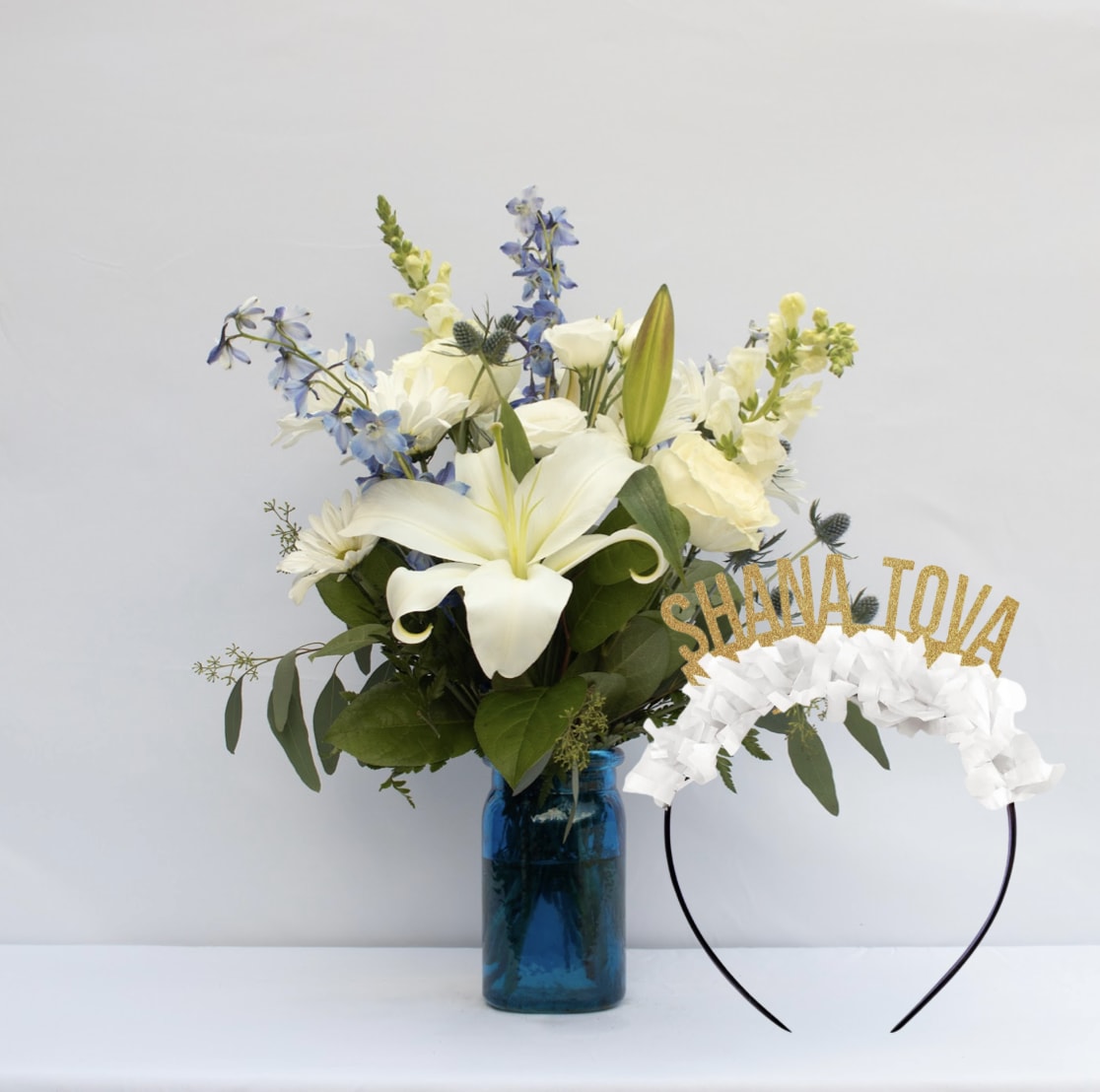 White lily bouquet in a blue glass vase with a Shana Tova headband