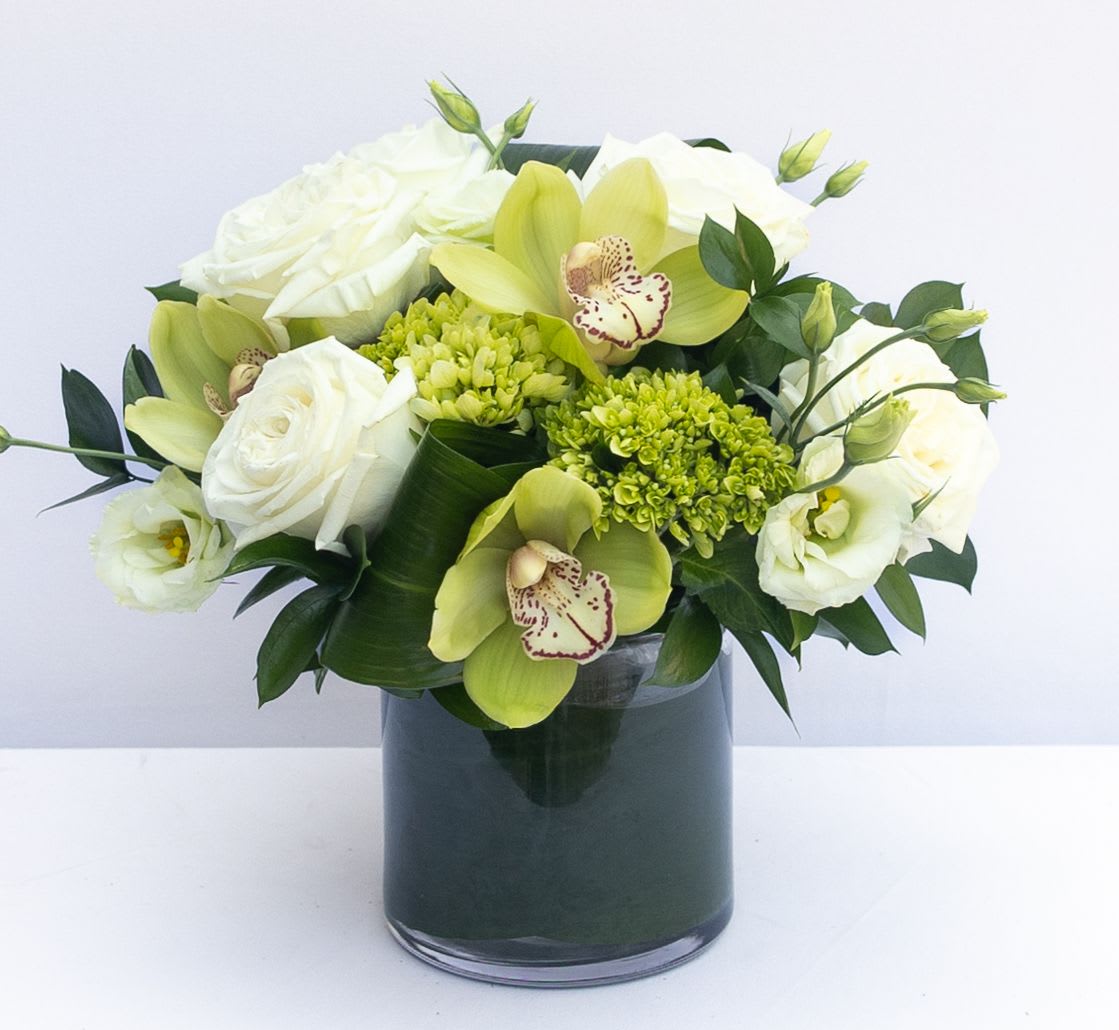 White roses and green orchids arranged in a dark glass vase