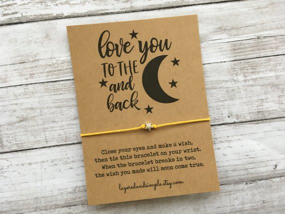 A card with a yellow string bracelet and moon graphic on a wood surface