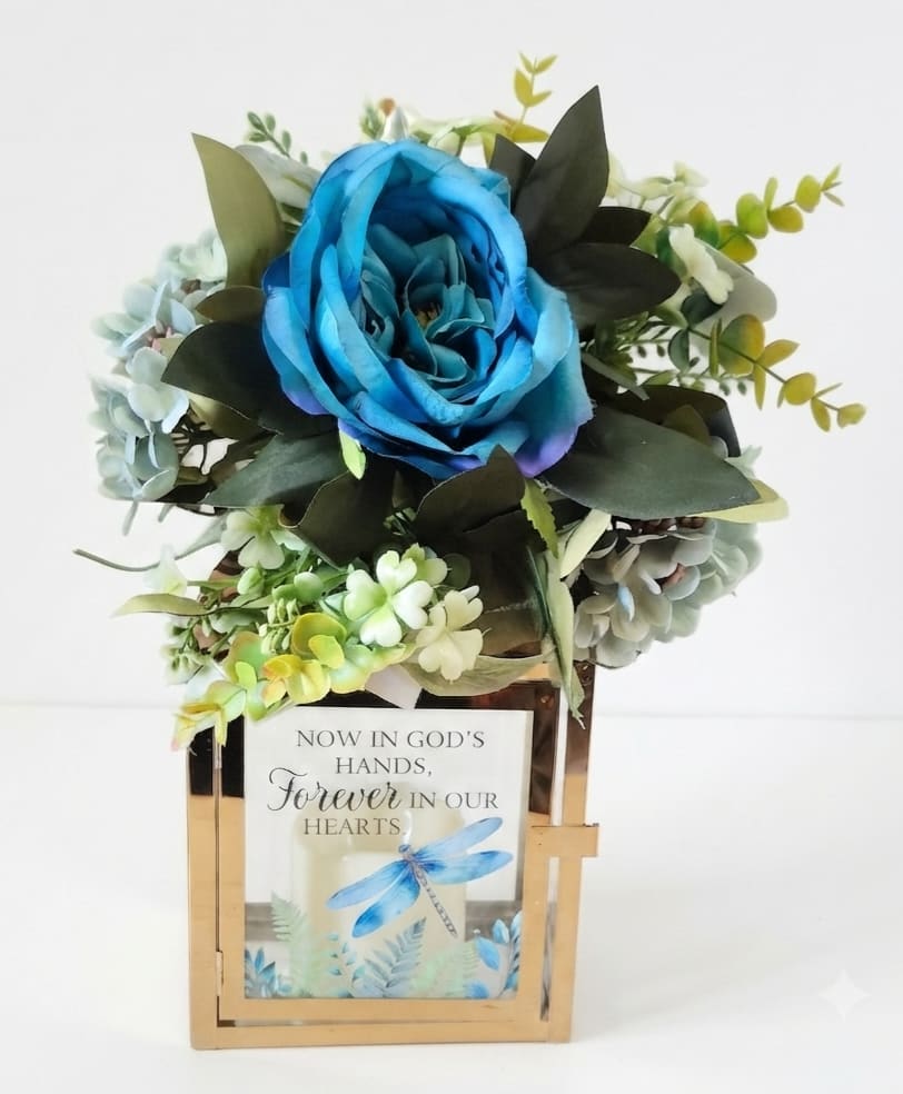 Blue rose arrangement in a gold lantern with a memorial card